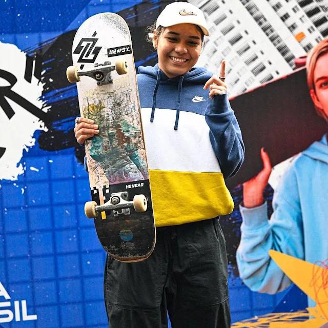 Daniela Vitória segura seu skate e faz o número 1 com a mão