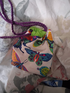 Drawstring bag, in butterfly print fabric, pulled closed. Casing and drawstrings are in coordinating but not matching colors. Drawstring is braided cotton worsted yarn.