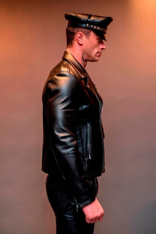 Knees up sideview of Leatherman sporting Muir cap and shiny leather jacket & pants