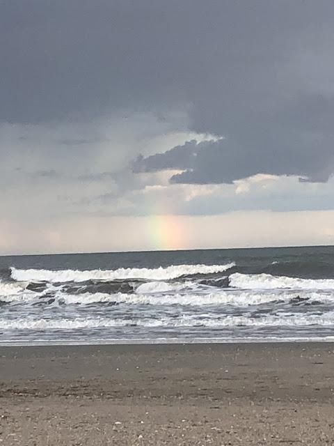 A better picture of the rainbow at it sits on the horizon. The dark clouds hang low in the sky. The waves are crashing with more power as the storm blows in.