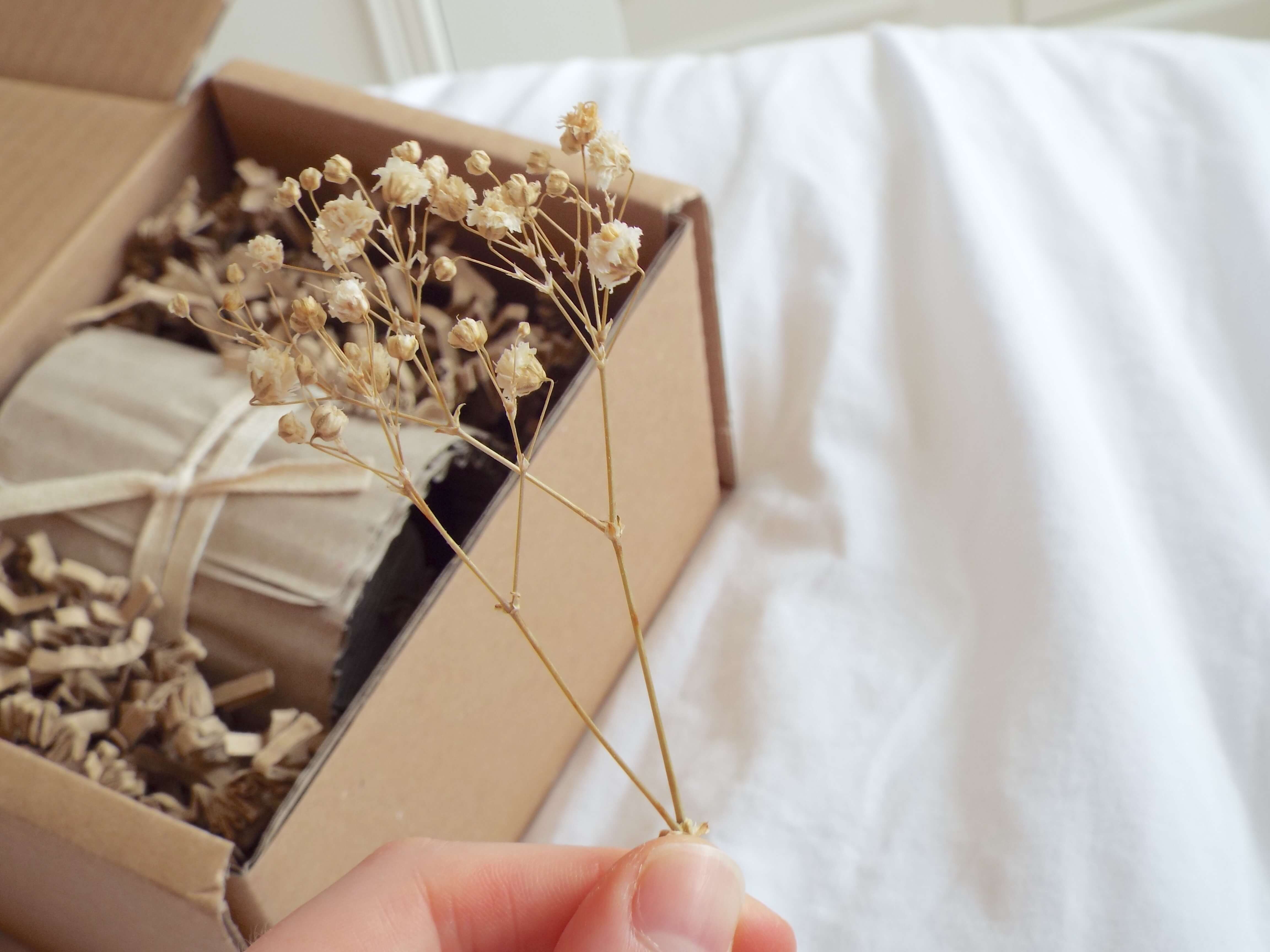 Holding the delicate beige dried flower above the box of the neatly nestled candle.