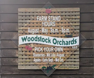 A sign mounted on a wall that reads "Woodstock Orchards" and the notes "Ausgust–may 9 a.m. – 6 p.m." and "Apples: Early Sept – Mid October"
