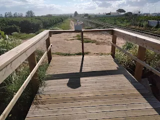 Boardwalk with railings, blocked by a fence, there is a hole in the fence on the left side.