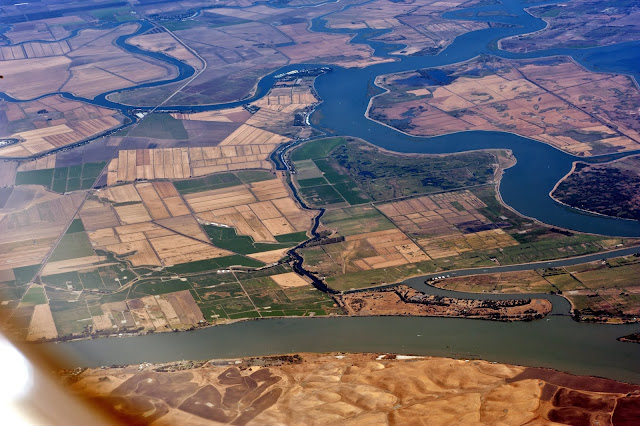 Aerial photo of farmlands, river/water channels and a bridge spanning the channel, located somewhere in the US.