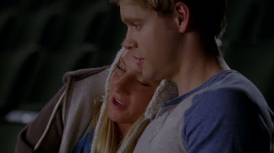 Brittany is resting her head on Sam's shoulder as they sit side by side in the auditorium