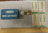 Small box marked "MSA First Aid Packet," 2 cylindrical containers, and 4 Curad brand bandaids