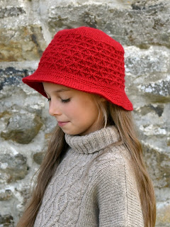 Girl is modelling in hand knitted hat in red color. The hat is knitted in shape of bucket hat with textured triangular stitch