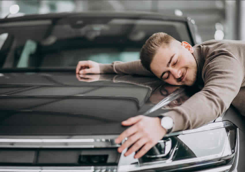 Imagem mostra um homem feliz dando um abraço em um carro.