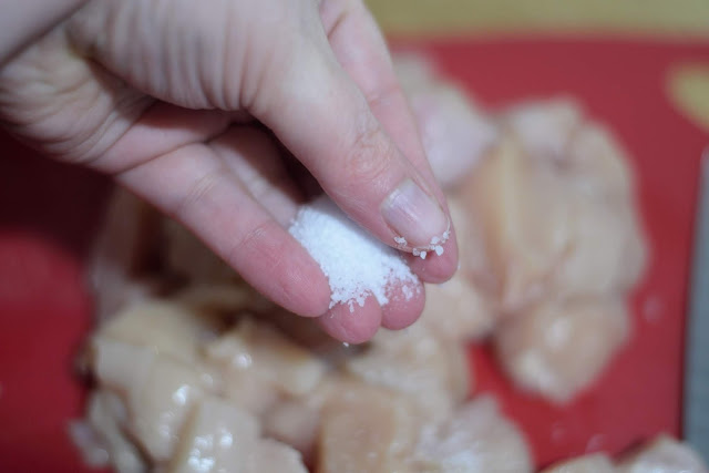 Raw chicken being seasoning with salt.