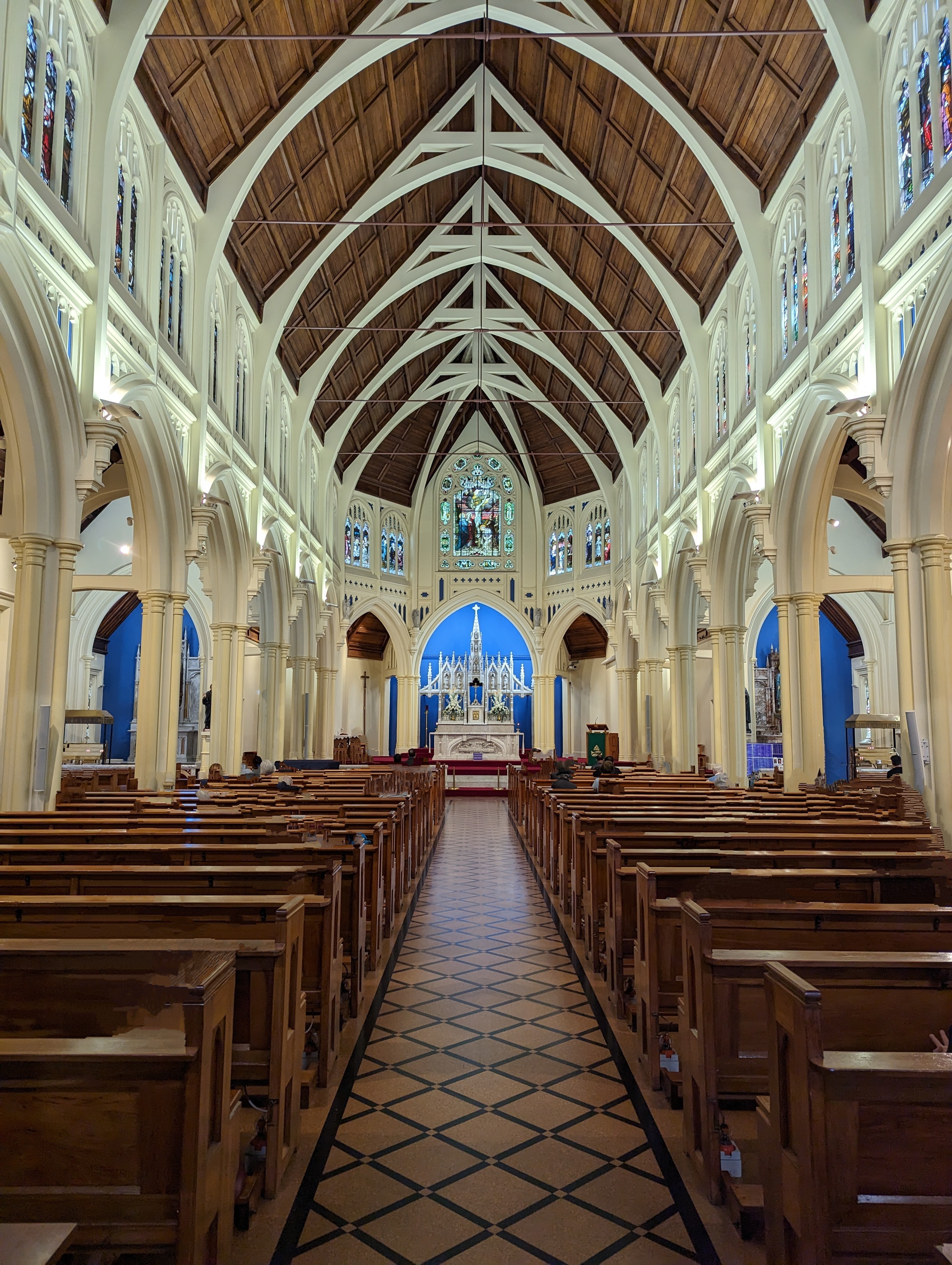 Inside of a large church looking down the aisle towards the altar. A large wooden roof with white spans covers empty pews where AI has removed all the people