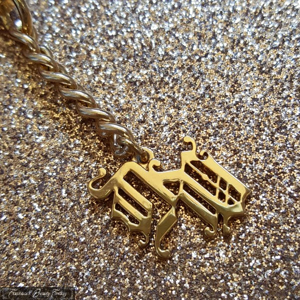 close up of gold charm detail on chain hanging from eyeshadow tube