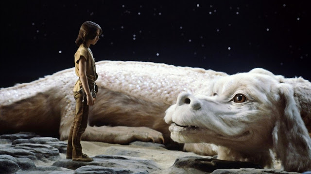 Film still from The Neverending Story. Atreyu is stood in front Falcor the Love Dragon.