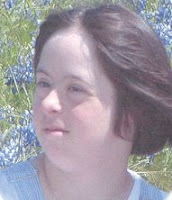 A headshot of a plump young white woman with short, dark hair gently blowing in the breeze, sitting in a field of bluebonnets