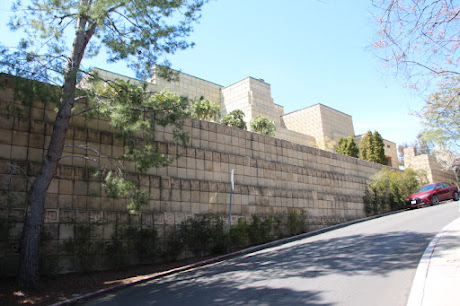 Photo of a two-toned concrete block wall on a hill enclosing an enormous house with complex massing, also made of concrete blocks.