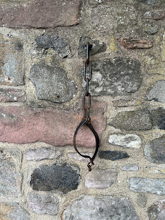 A photo of a black, iron collar attached to a stone wall - these are the jougs.   Photo by Kevin Nosferatu for the Skulferatu Project.