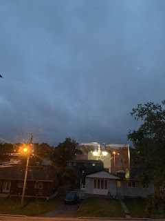 A near photo of a street, aiming above the houses at the fast moving clouds. A street light is on to the left of the scene.