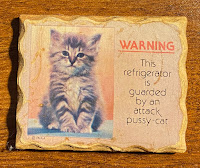 A plaque with the words, "Warning: This refrigerator is guarded by an attack pussy cat. There is a photo of a cat.