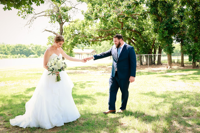 A very special wedding took place on May 19, 2018…besides the one 'across the pond' with Prince Harry and Meghan!  After a five-year engagement, Liz and Chris tied the knot at Stillwater Bible Church, where the couple are regular attendees.      If there is one thing we know about Chris, it is that he is persistent.  Chris said it took him six months to get Liz to start talking to him after first meeting in a sophomore speech class in college.  But from then on, they have become inseparable.  Liz shared that Chris proposed to her at Sandborn Lake as they watched the multi-colored Oklahoma sunset disappear.  It was an "intimate, private moment…special and perfect."  There's no doubt these two were made for each other.        On their wedding day, Liz was stunning in her strapless wedding gown, composed of light and airy tiers of tulle below a perfectly shaped bodice.  Her bridesmaids wore romantic, dusty blue chiffon gowns and carried white hydrangeas, while the bride's bouquet included white roses, baby's breath, snapdragons and hydrangeas with blue accent flowers.  Chris looked dapper in his royal blue suit, dusty blue tie, and two-tone brown, intricately stitched cowboy boots (the bride had cowboy boots on too).      After they exchanged vows, guests were invited to a reception buffet, the cake cutting, and the first dances.  The day was filled with heartfelt moments shared by the people they loved, and before long, the young couple departed amid a throng of well-wishers…headed for a romantic getaway honeymoon to Yellowstone and the Grand Tetons.  Wishing you two a lifetime of love and romantic nights watching the sunset by Sandborn Lake!