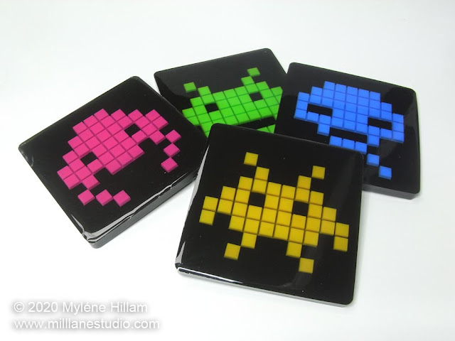 Set of 4 square resin space invaders coasters with pink, green, blue and yellow pixelated aliens on a black background