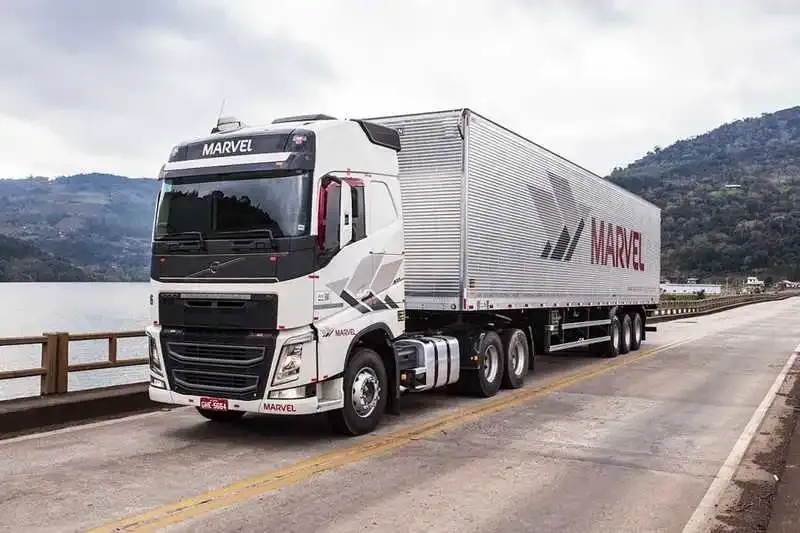 Volvo FH com carreta baú passando em ponte sobre rio