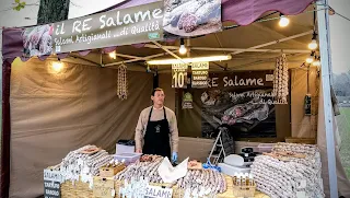 Immagine che ritrae la vivace atmosfera del November Porc 2024, con bancarelle piene di prelibatezze locali come il Culatello di Zibello e la Spalla Cotta di San Secondo. Sullo sfondo, la tipica nebbia della Bassa Parmense avvolge i borghi di Sissa, Polesine Parmense, Zibello e Roccabianca. I visitatori si immergono in un mix di sapori, tradizione e festa.