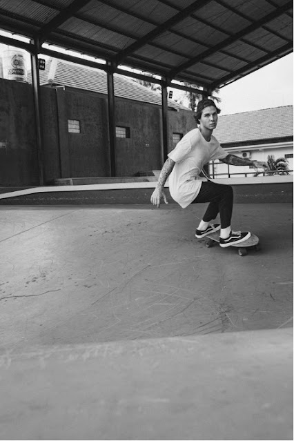 back and white image of person wearing white t shirt and baseball cap backwards skateboarding