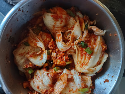 Kimchi in preparation: Napa cabbage that has been cut in quarters, salted, and dressed with a red sauce, fermenting in a stainless steel bowl