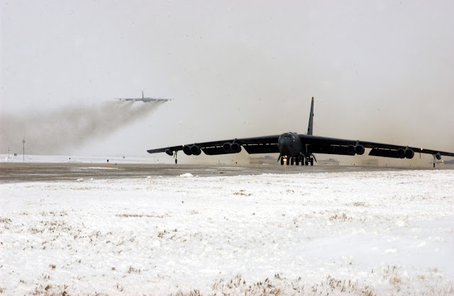 A B-52 Stratofortress taxis down the runway while another B-52 takes of in the background.