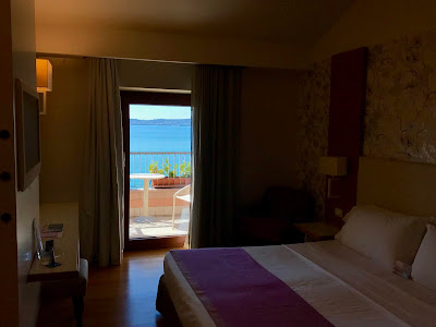 Hotellrom med dobbeltseng. Åpen balkongdør med sjøen i bakgrunnen.
