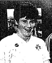 A smiling woman with short dark hair and a white football shirt