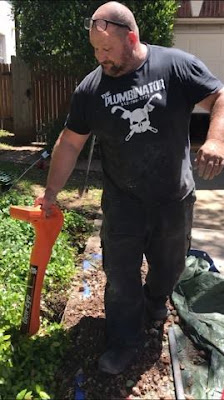 A plumber uses a long orange tool, pointing the nose at the ground, listening for it to make a noise that indicates a leak
