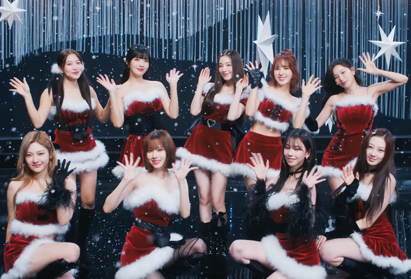 [From left to right: Ningning, Joy, Yeri, Winter, Irene, Wendy, Karina, Seulgi, Giselle] Red Velvet and Aespa posing together with their hands up, wearing Santa Claus inspired outfits, on a navy blue and silver snow themed set.