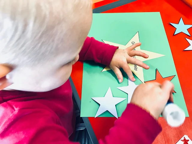 A toddler sticking paper stars on to card with pritt stick