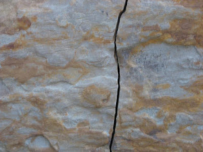 Detail of a reddish stone block with a human-created crack running from top to bottom