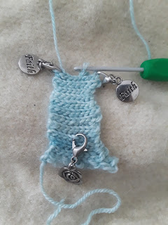 a small strip of crochet ribbing worked in fingering-weight pale blue yarn.  A silver rose stitch marker is clipped into the fabric, while two other stitch markers are clipped in at each end of the row.