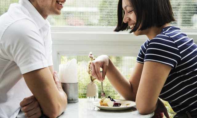 カフェで歓談する若い男女。女性をケーキを食べている。