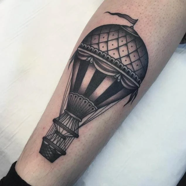 Brazo con un tatuaje de globo aerostático en tonos grises estilo antiguo