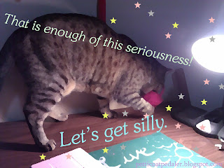 Photo of a cat on a desk top with a crochet toy in her mouth.  The photo is edited to look like a very detailed oil painting and then has stars scattered over it.  There are words across the picture and they read: That is enough of this seriousness.  Let's get silly.  