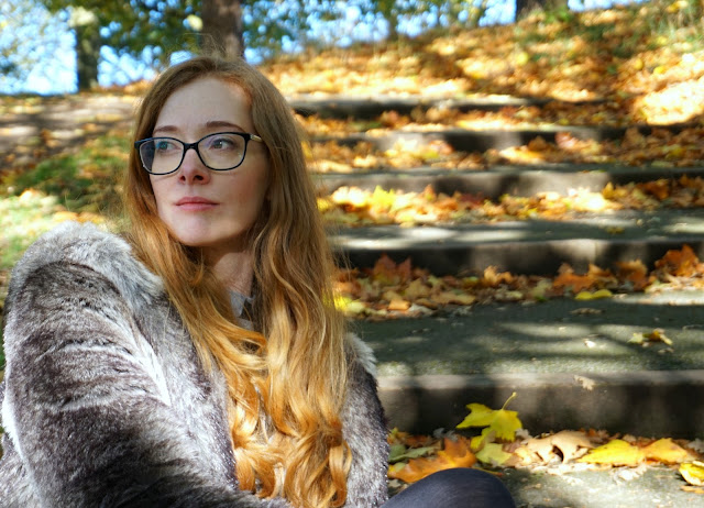 autumn photo of redhead wearing glasses and sitting outside on stone steps looking off camera