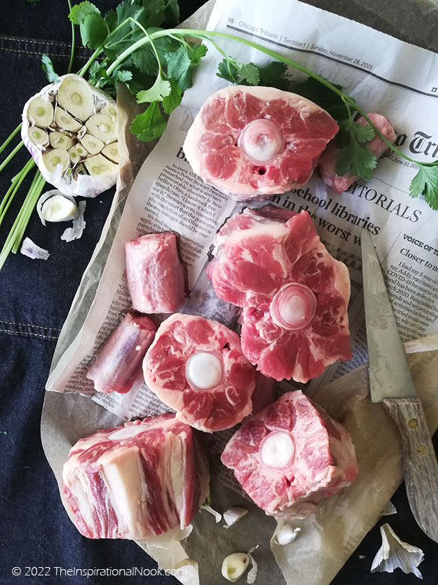 Freshly cut oxtails on a newspaper with cut garlic, green coriander leaves and a wooden knife