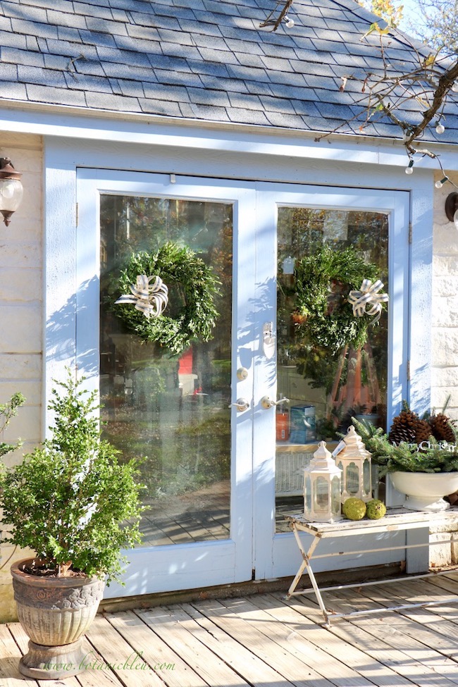 Inexpensive fresh boxwood wreaths hang on the French doors of the French Country Christmas garden shed