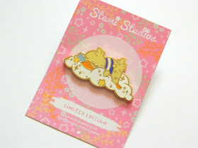 A photo of a pin badge, a sleeping duck on a fluffy white cloud. the pin has a shiny gold outline