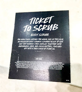 A black rectangular card with Ticket To Scrub in big white font with Body Scrub in smaller white font with very small details of the ingredients in white font on a white background 