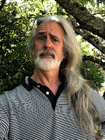 A man with long grey hair and a beard looking perplexed.