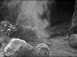 An alien vaguely resembling an alligator, lying on the ground with smoke coming from it.