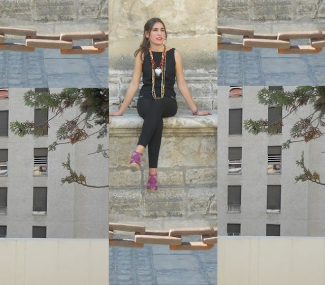 composición fotográfica. Una joven sentada mirando al infinito con las piernas cruzadas y un largo collar. Edificios altos y una cadena.