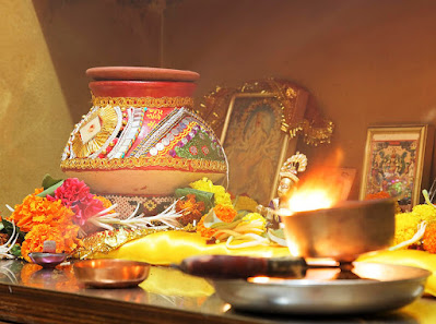 A Hindu devotion table, featuring images of Hindu gods, colorful flowers, metal trays and bowls, and a flame.