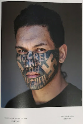 Portrait of a man's face with prominent tattoos, including swastikas.