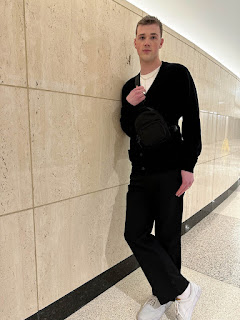 Isaac leaning against a wall wearing a black sweater and pants.