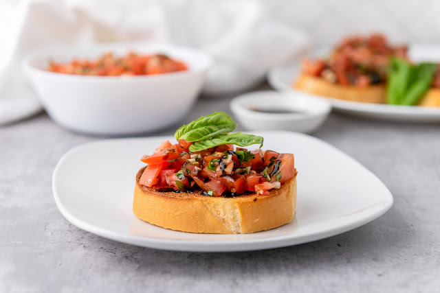 Bruschetta on toast on a white plate with gray background.